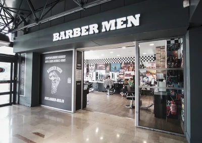 Façade intérieure du salon BARBER MEN à Aubagne, avec l'enseigne lumineuse visible depuis le sas d'entrée de la galerie.