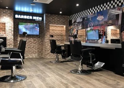 Intérieur du salon BARBER MEN à Istres : postes de coiffage, enseigne néon, vitrine et TV.