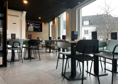 Vue de l’espace restaurant de L’Acte 08, mettant en avant un mobilier moderne, de grandes baies vitrées et un affichage dynamique au fond de la salle.