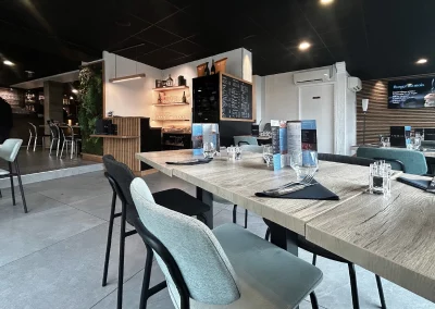 Vue de la salle du restaurant L’Acte 08 avec des tables élégamment dressées, un mobilier moderne et l’espace bar visible en arrière-plan à gauche.
