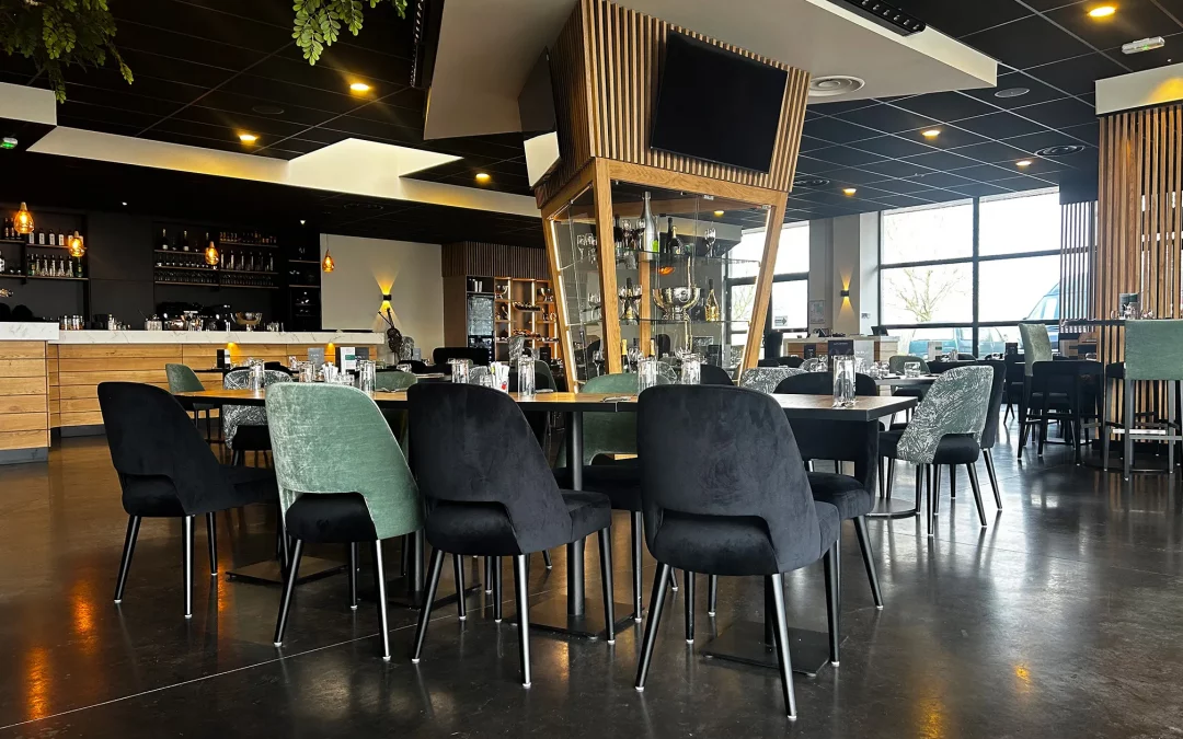 Vue intérieure du restaurant L’Acte 24 mettant en avant le meuble à champagne central, le design élégant des chaises et l’ambiance chaleureuse du bar.