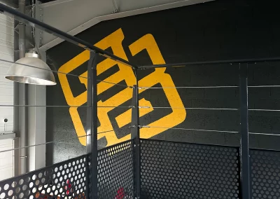 Vue depuis la mezzanine du bar Beer Or Not To Beer, mettant en avant un mur noir avec le logo jaune peint et une structure métallique industrielle.