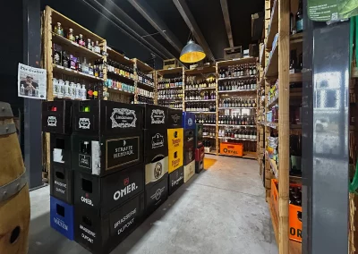 Vue de l’espace cave à bière de Beer Or Not To Beer, mettant en avant des étagères en bois remplies de bouteilles artisanales et des caisses de grandes brasseries.