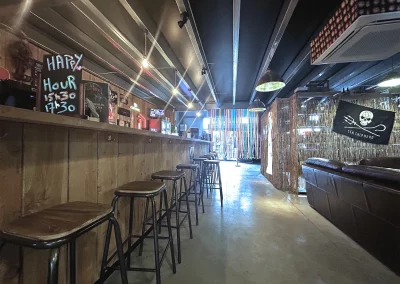 Vue intérieure de Beer Or Not To Beer avec, à gauche, un long comptoir en bois et ses tabourets, et à droite, un espace détente avec canapés en cuir et décoration immersive.