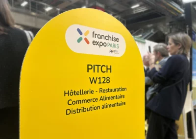 Panneau du pitch W128 consacré à l’hôtellerie, la restauration et le commerce alimentaire au salon Franchise Expo Paris.