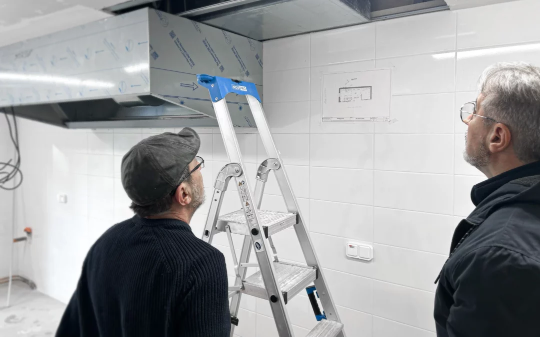 Maître d’œuvre et artisan analysant l’installation d’une hotte dans une cuisine professionnelle en chantier CHR