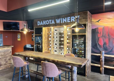Espace Dakota Winery avec présentoir à bouteilles, caves à vin intégrées et grande table haute en bois pour les dégustations.