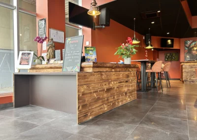 Comptoir d'accueil en bois du Dakota Café avec tableau du plat du jour, plantes décoratives et tables hautes en arrière-plan.